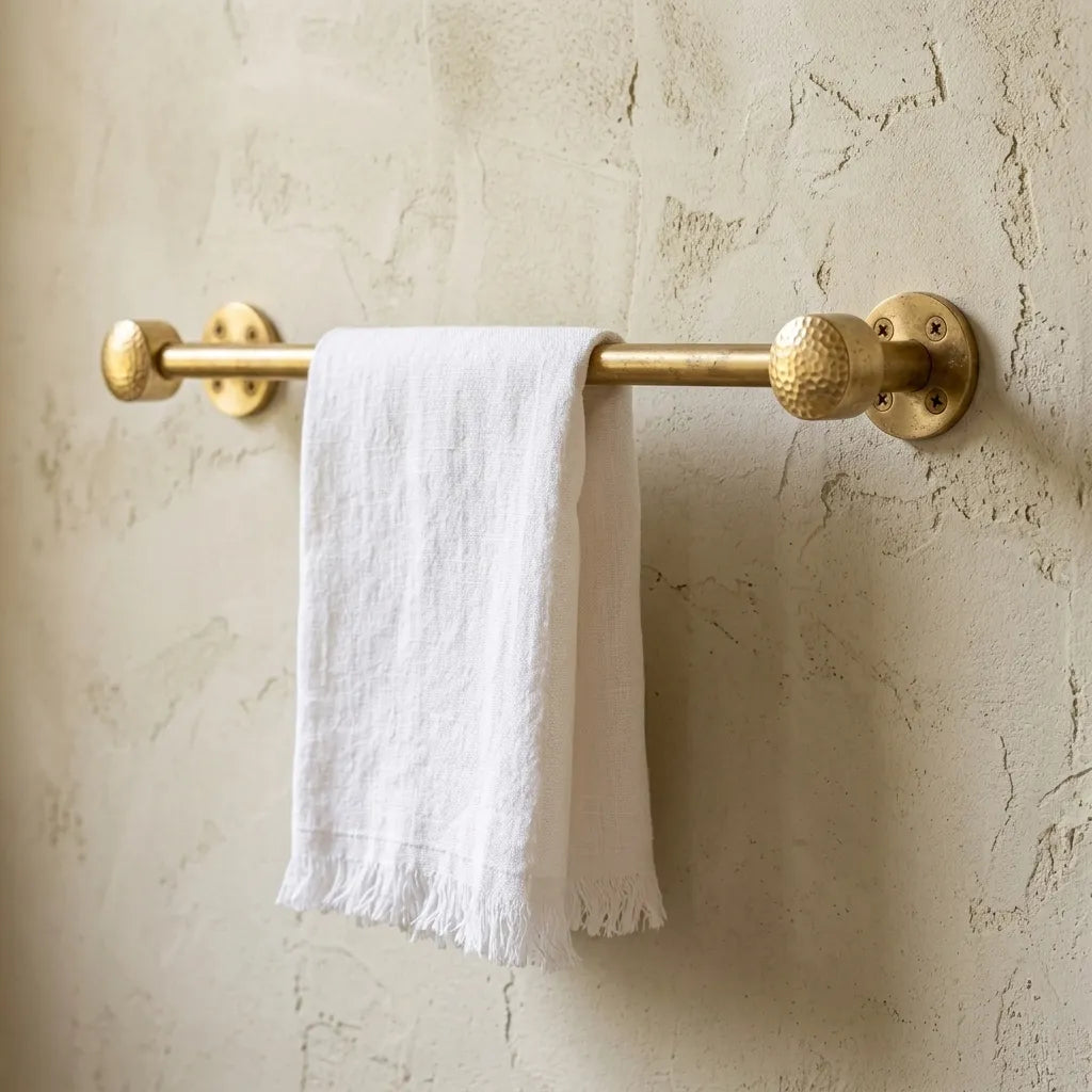 Solid brass towel bar with hammered end caps mounted on textured plaster wall