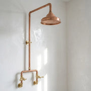 Handcrafted outdoor copper rain shower with exposed copper pipework, solid brass cross handles, and a large round copper shower head for rustic garden and poolside bathrooms.