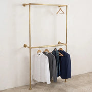 Solid brass floor to wall garment rack with double hanging rails for open wardrobe storage.