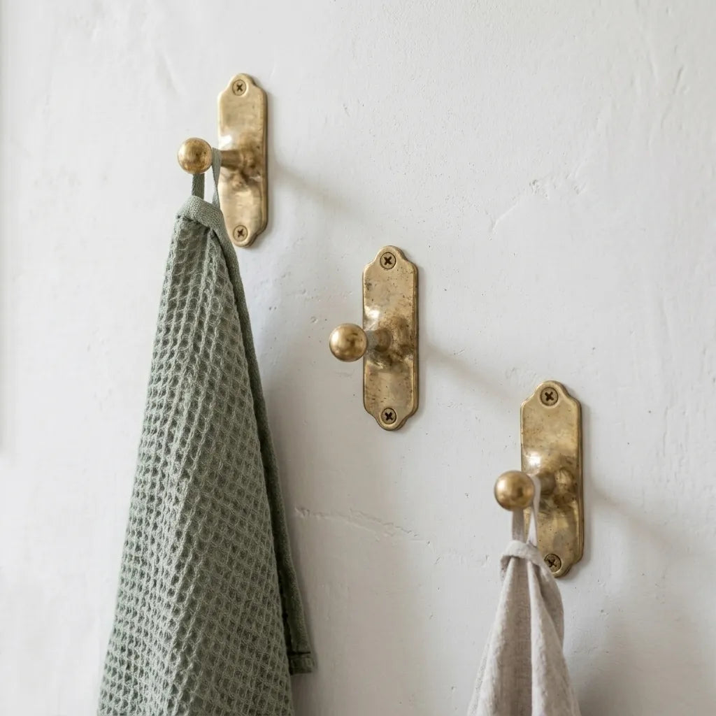 Solid brass wall hook with decorative backplate mounted on a white wall holding kitchen and hand towels.