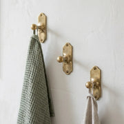 Solid brass wall hook with decorative backplate mounted on a white wall holding kitchen and hand towels.