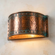 Handcrafted hammered copper wall sconce with verdigris riveted trim and curved shade.