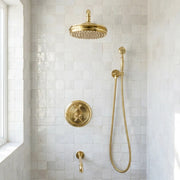 A luxury brass shower fixture set installed in a white tiled bathroom corner, featuring a round rain shower head, handheld shower with hose, a round control plate, and a wall-mounted valve.