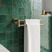A double-bar brass towel bar mounted on a glossy green tiled bathroom wall, with a white waffle-weave towel hanging from it.