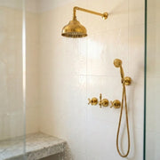 Unlacquered brass wall shower system with domed rain shower head and handheld shower installed in a tiled walk-in shower.