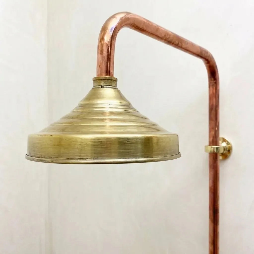 Handcrafted brass rainfall shower head mounted on exposed copper pipe with vintage industrial styling