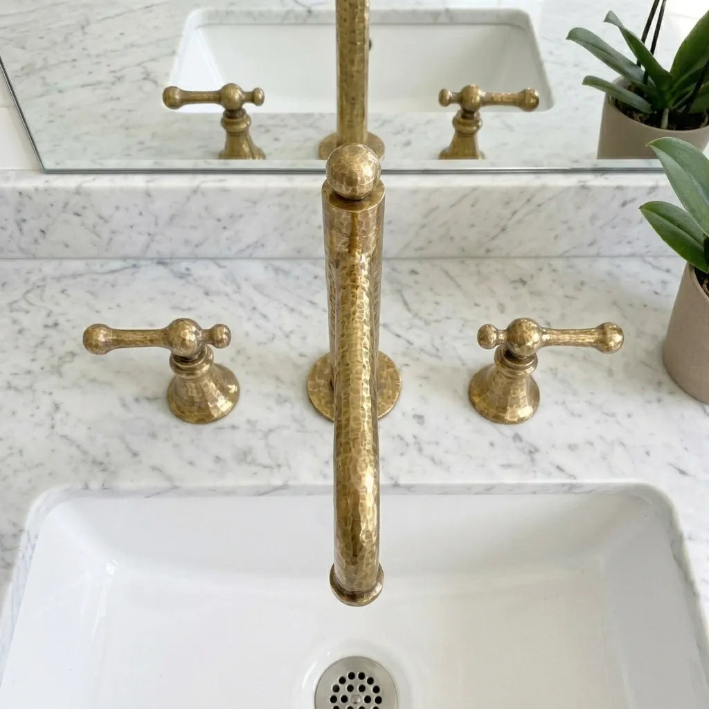 Hammered brass vanity faucet with elevated bridge spout and handcrafted detailing beside a white basin