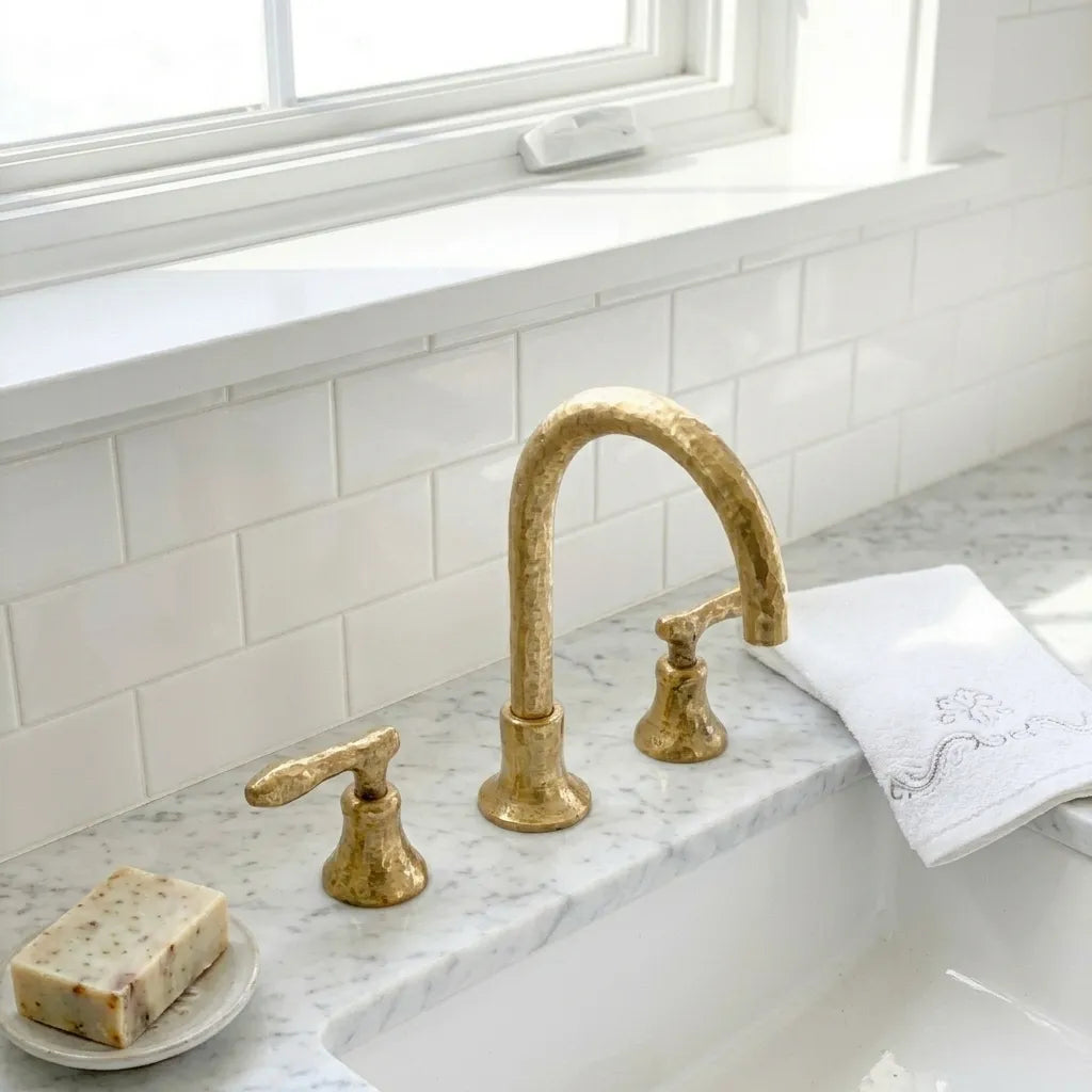 Textured brass vanity faucet with dual lever controls and handcrafted metalwork beside a white basin