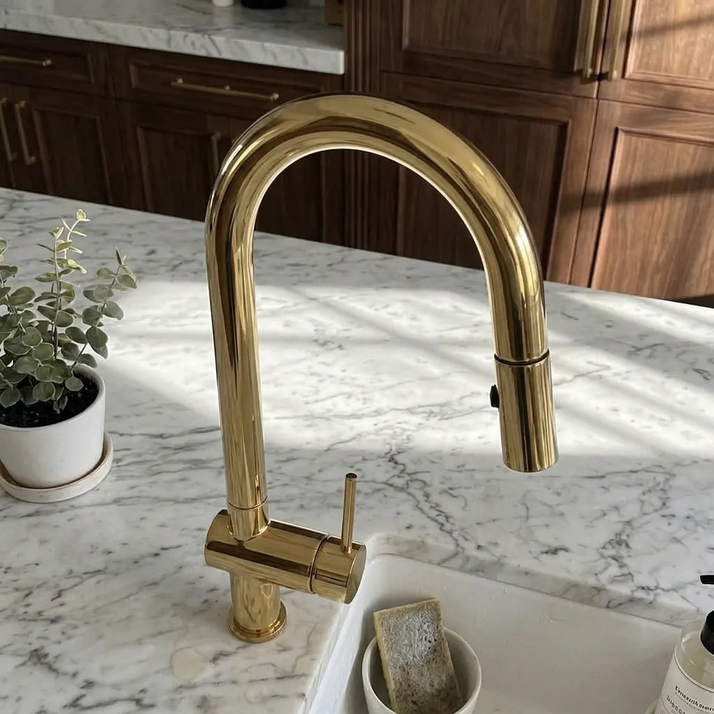 A polished gold kitchen faucet with a curved high-arc spout and single lever handle, installed on a white marble countertop in a kitchen with dark wood cabinets.