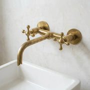 Unlacquered brass wall mount bathroom faucet with cross handles and an extended spout, designed for vessel sinks and custom vanities