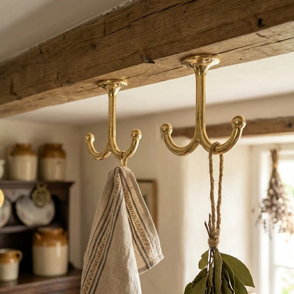 Handcrafted brass double utility hook mounted under a reclaimed wood beam for farmhouse kitchen storage.