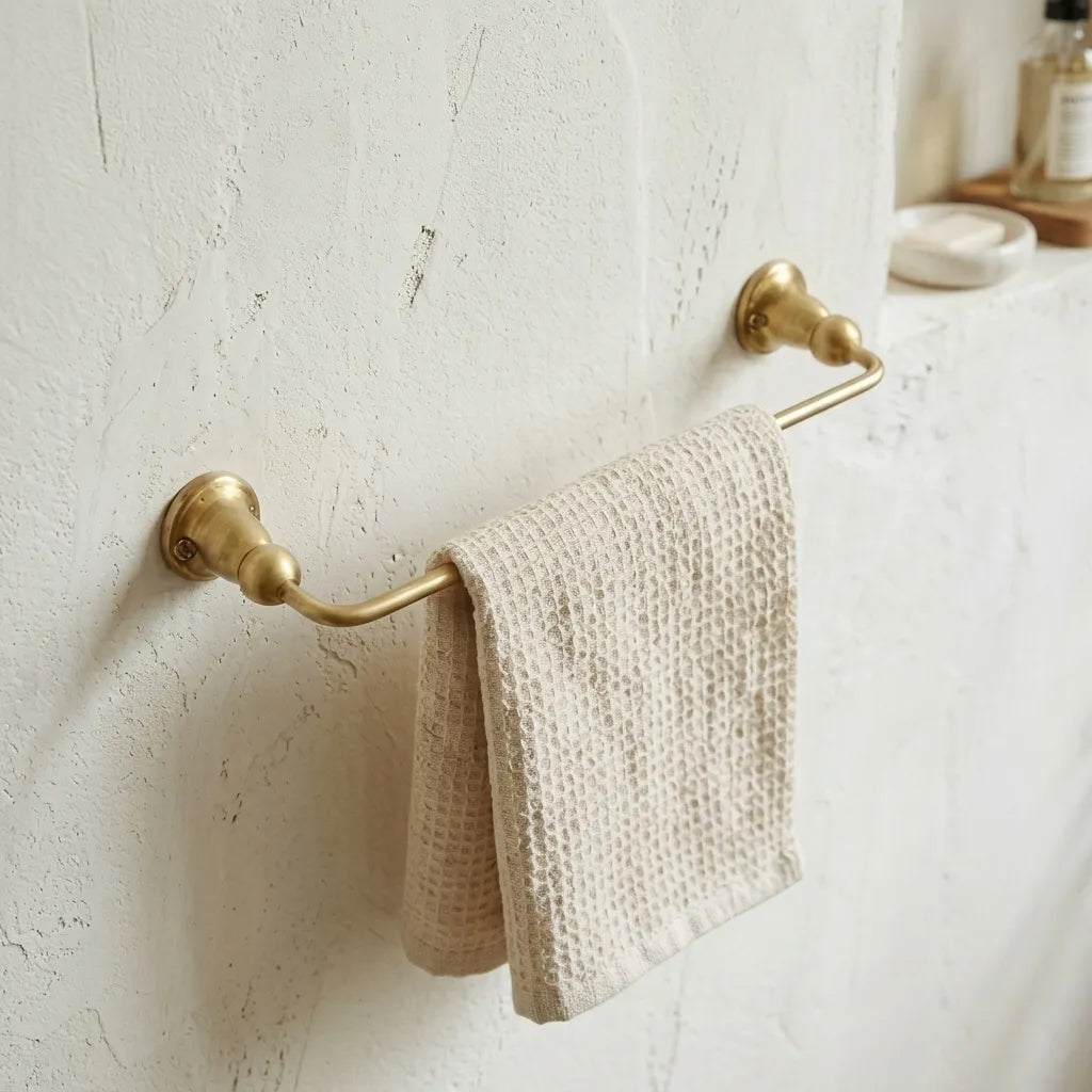 Unlacquered brass hand towel bar mounted on a textured bathroom wall with a soft woven towel draped across the rail