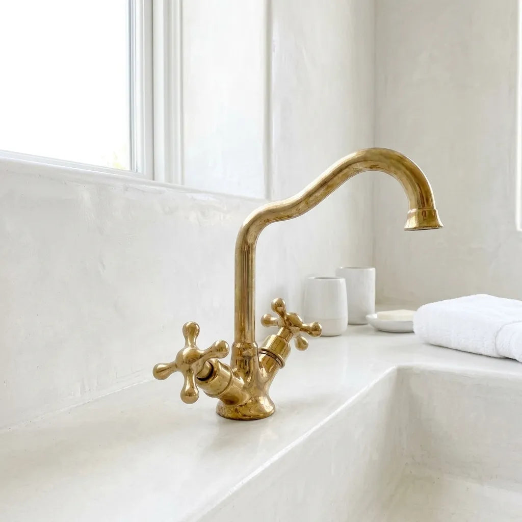 Vintage brass bathroom faucet with cross handles and elegant swan neck spout beside a handcrafted sink