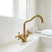 Vintage brass bathroom faucet with cross handles and elegant swan neck spout beside a handcrafted sink