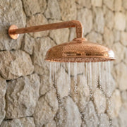 Hammered Copper Outdoor Rain Shower Head with Wall Mounted Arm on Stone Wall