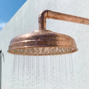 Handcrafted hammered copper rain shower head with wall-mounted arm creating a relaxing rainfall shower experience.