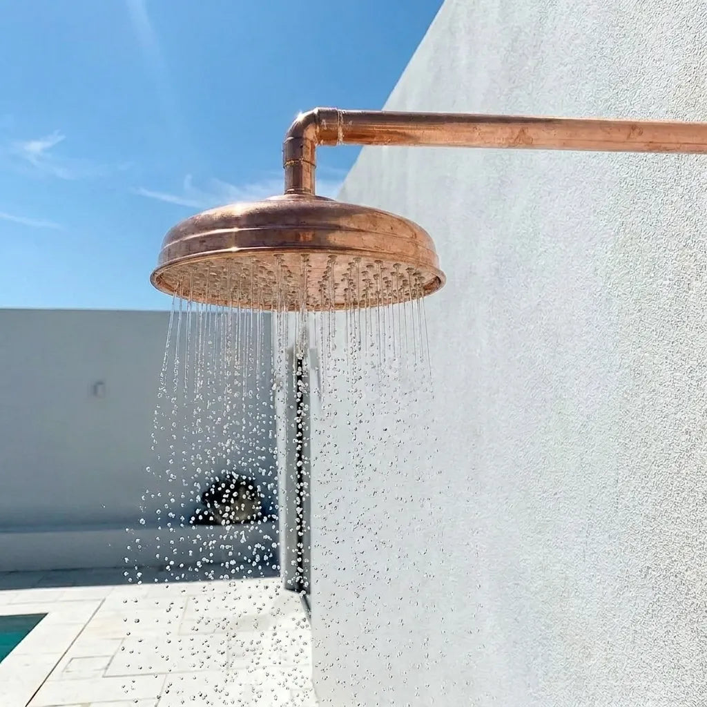 Solid copper round rain shower head with hammered finish and exposed wall arm for luxury bathroom or outdoor shower.