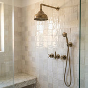 Vintage unlacquered brass wall mount shower system with domed rain shower head, handheld sprayer, and concealed controls.