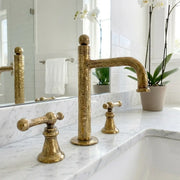 Hand hammered brass bathroom faucet with widespread lever handles and architectural spout on a marble vanity