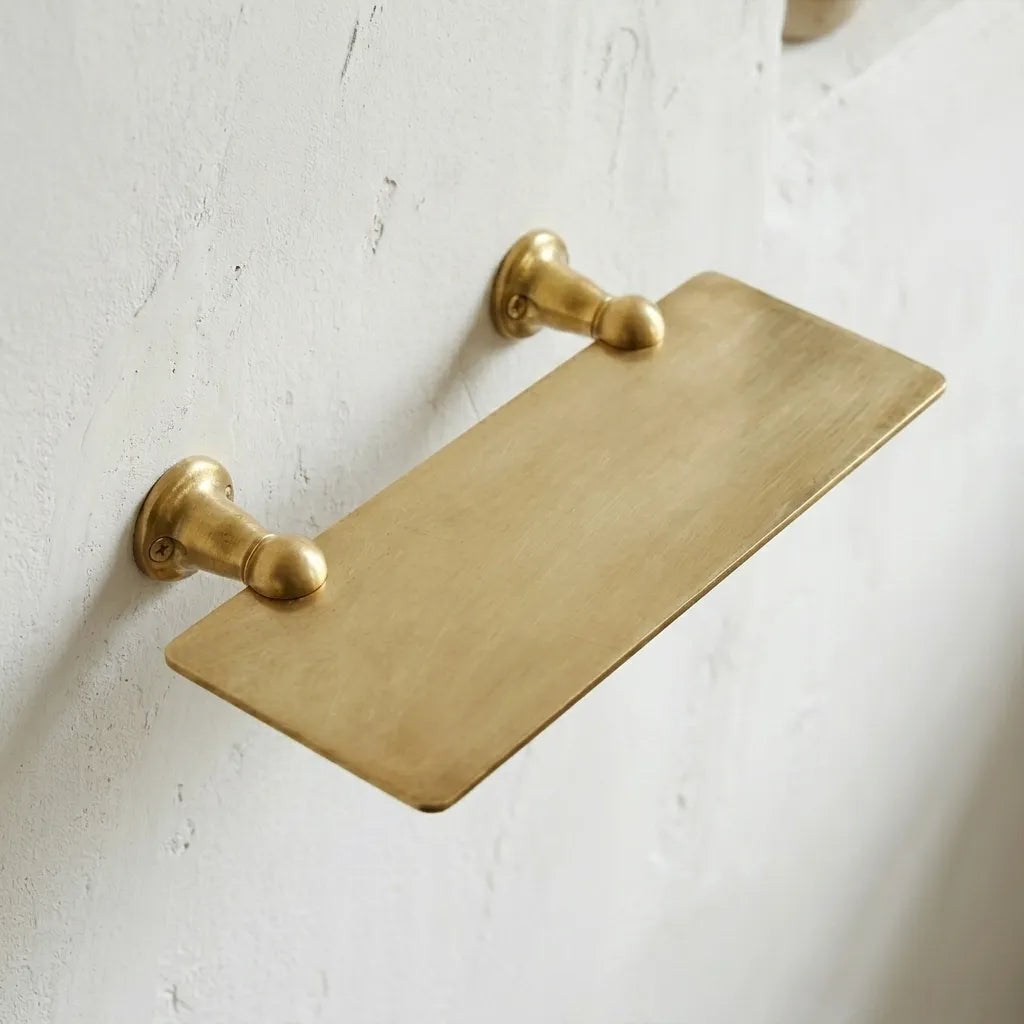 Unlacquered brass wall shelf with a slim rectangular profile, designed for bathroom essentials, candles, and decorative accessories