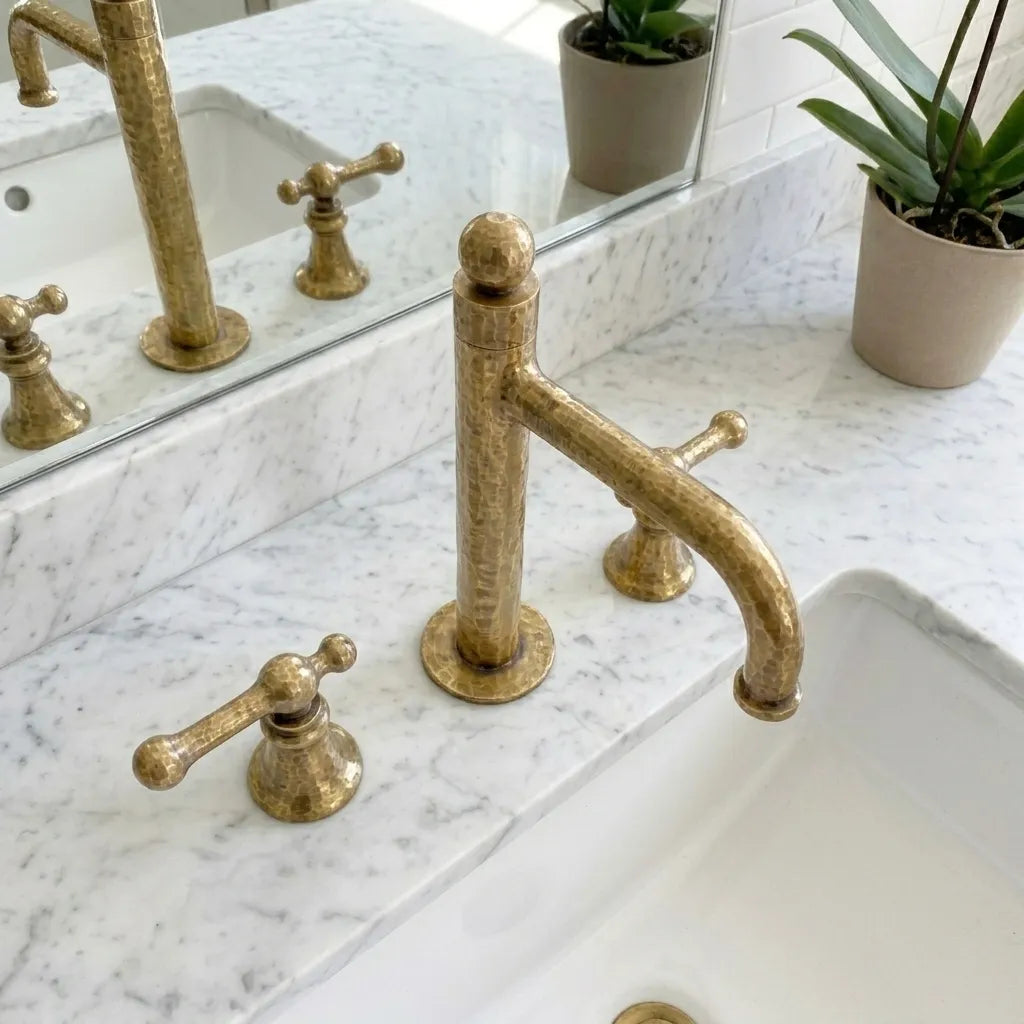 Artisan forged brass sink mixer featuring textured metalwork and dual handle controls in a luxury bathroom