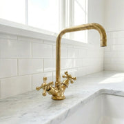 Traditional brass bathroom faucet with square gooseneck spout and cross handles installed on a marble vanity countertop