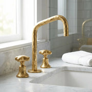 Hammered brass widespread bathroom faucet with geometric high arc spout and artisan textured finish on a marble countertop