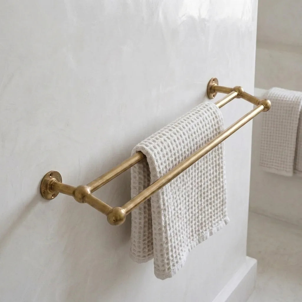 Solid brass double towel bar with rounded ball-end supports mounted on a bathroom wall, holding a textured white waffle towel.