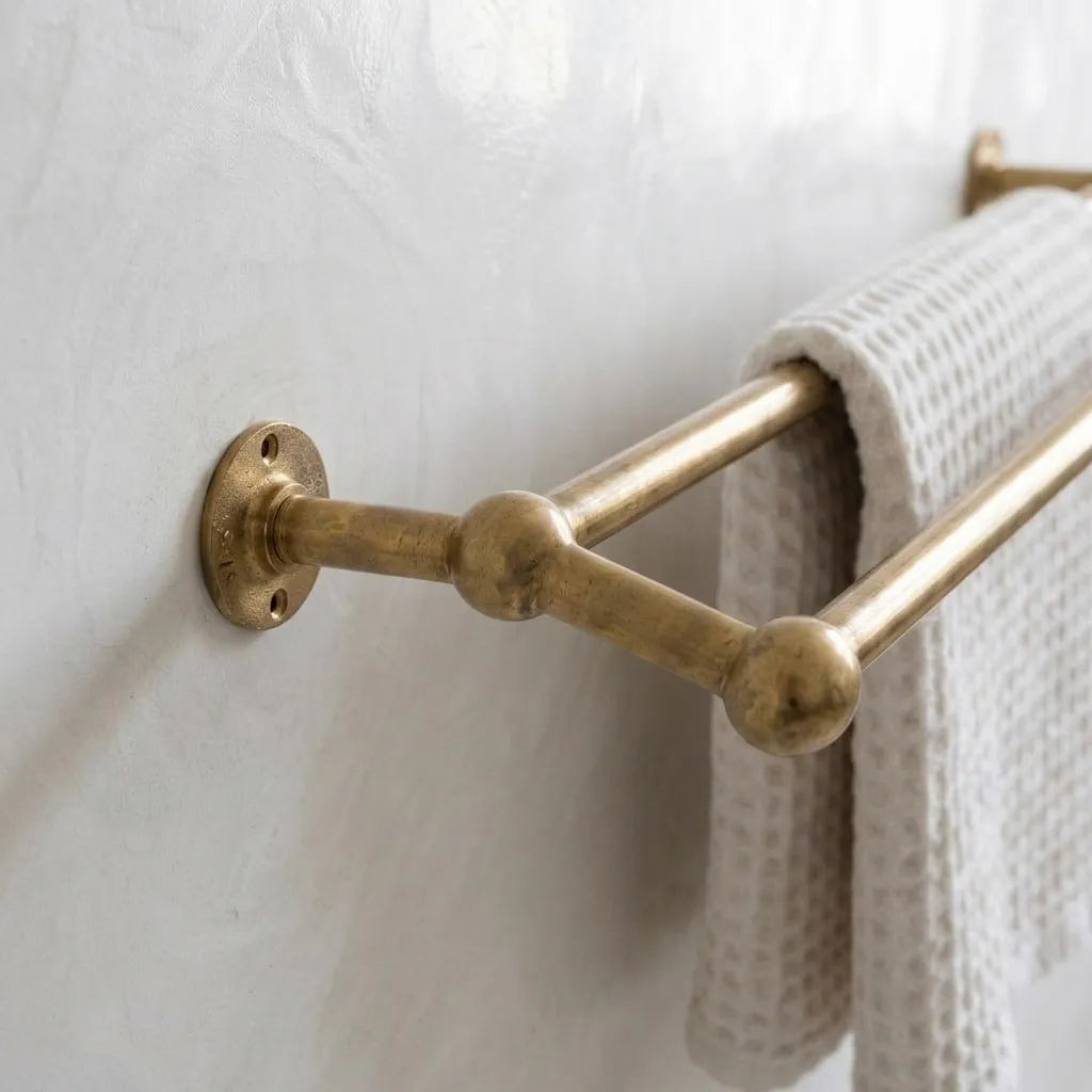 Close-up of a handcrafted unlacquered brass double towel rack highlighting the rounded connector joints and wall mounting plate.