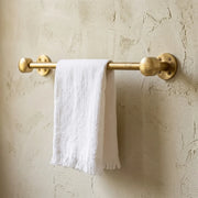 Solid brass towel bar with hammered end caps mounted on textured plaster wall