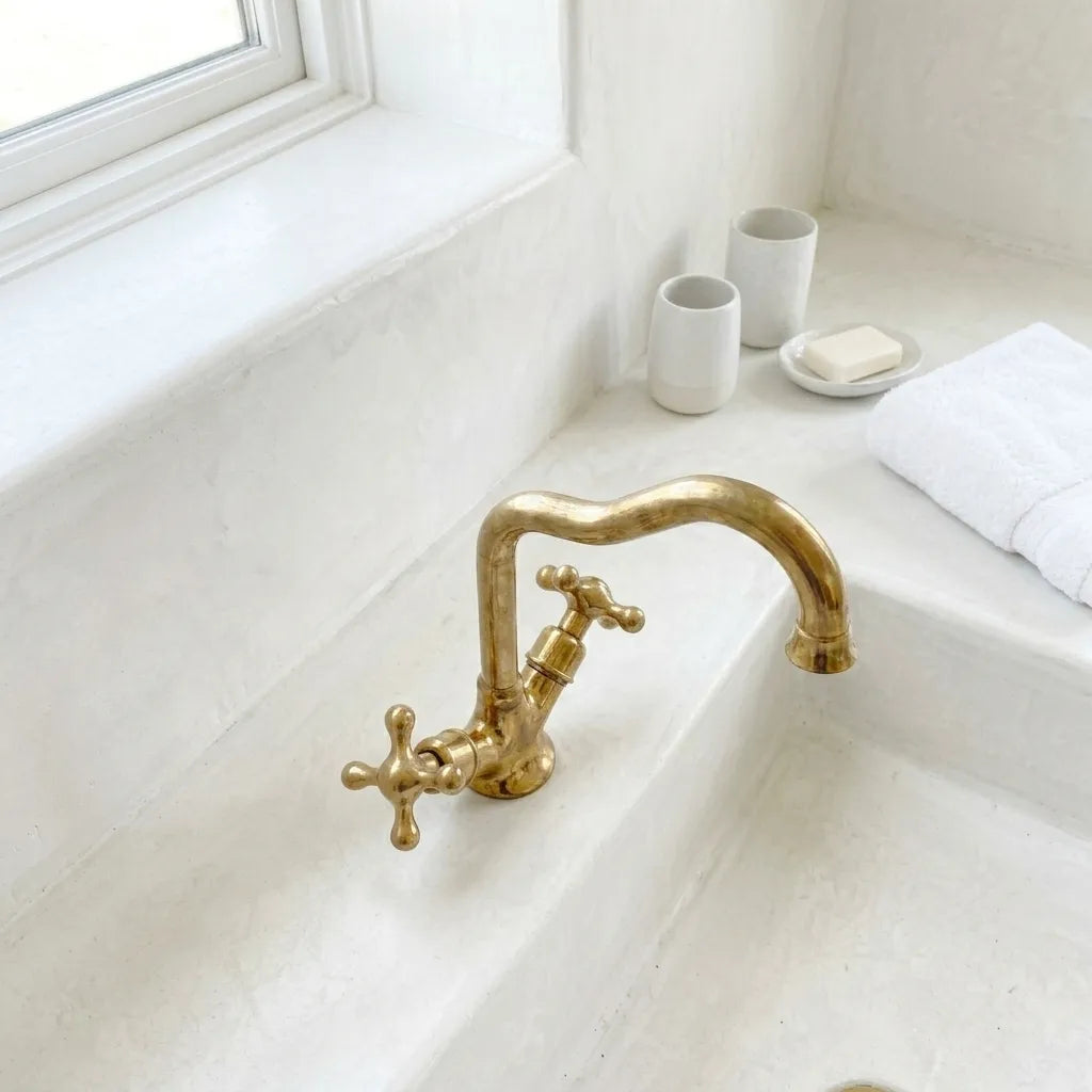 Classic brass basin mixer tap with high arc spout and decorative cross handles in a bright bathroom setting