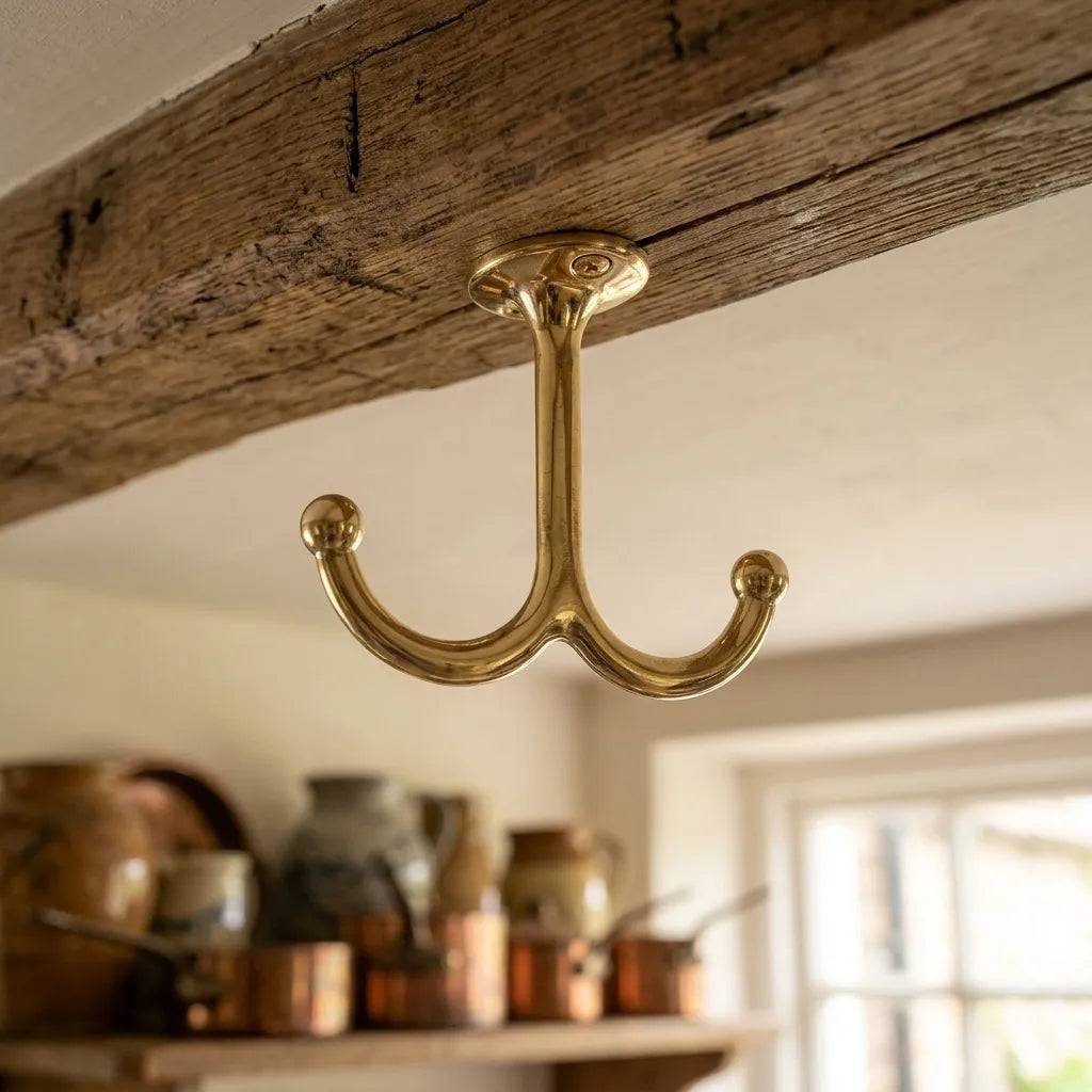 Solid brass ceiling-mounted double hook installed beneath a rustic wooden shelf for hanging cookware and kitchen accessories.