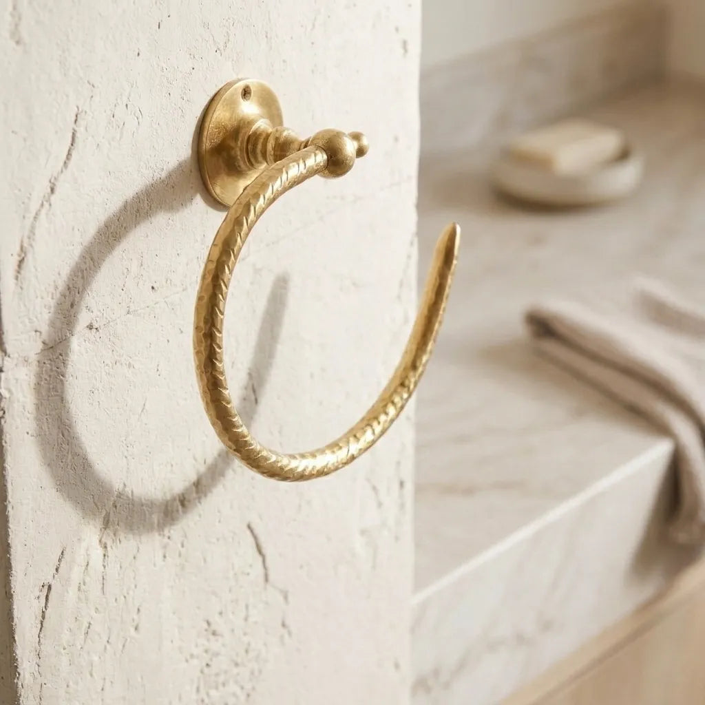Hand-hammered solid brass open towel ring mounted on a textured bathroom wall