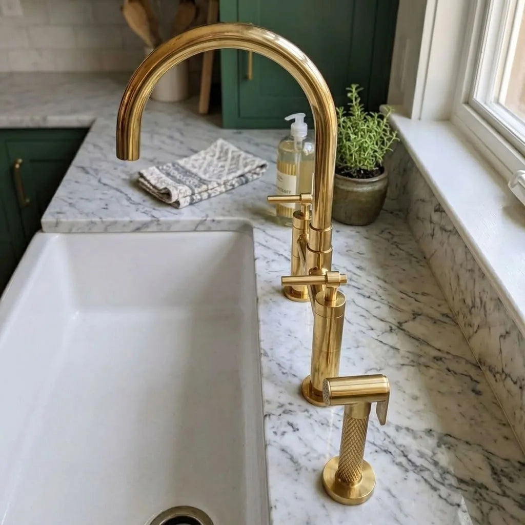 A three-hole faucet set installed in a white undermount sink on a white and gray marble countertop, with green cabinets and a small potted plant in the background.