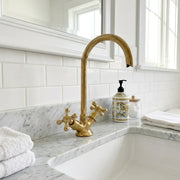 Traditional brass bathroom sink faucet featuring dual cross controls and an elevated curved spout beside a farmhouse basin