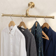 Solid brass ceiling mounted clothes rail suspended above hanging garments.