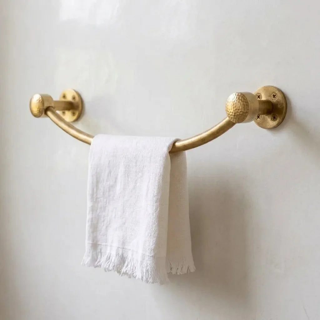 Wall-mounted arched brass towel rail with textured finials holding a white hand towel