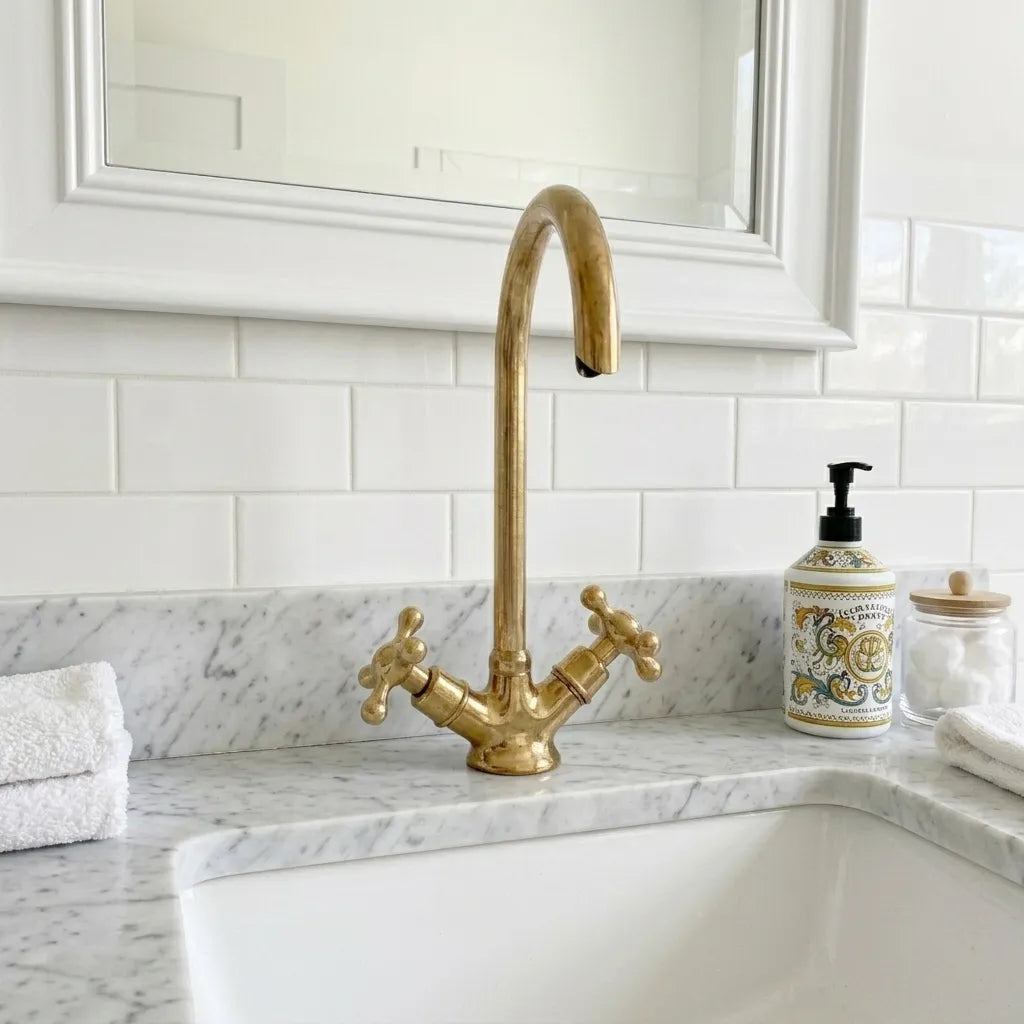 Unlacquered brass bridge faucet with cross handles and tall gooseneck spout installed on a marble bathroom countertop