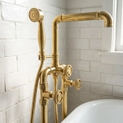 A vintage-style brass bathtub faucet set with a handheld shower head, flexible hose, and control valves, installed against a white subway tile wall next to a white bathtub.