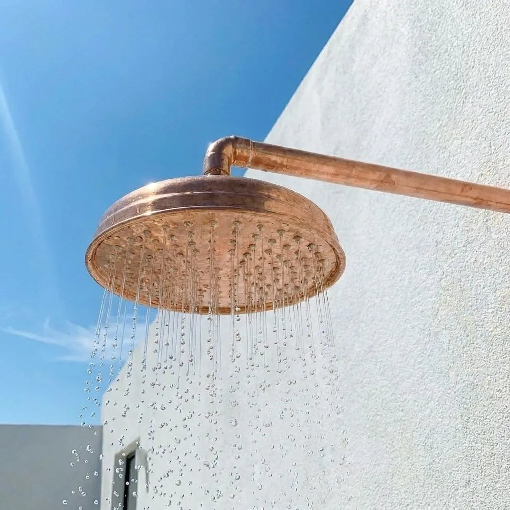 Vintage-style hammered copper shower head with wall-mounted pipe delivering a spa-inspired rainfall water flow.