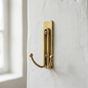 Solid brass double wall hook with minimalist backplate for hanging towels, robes, coats, and bags.