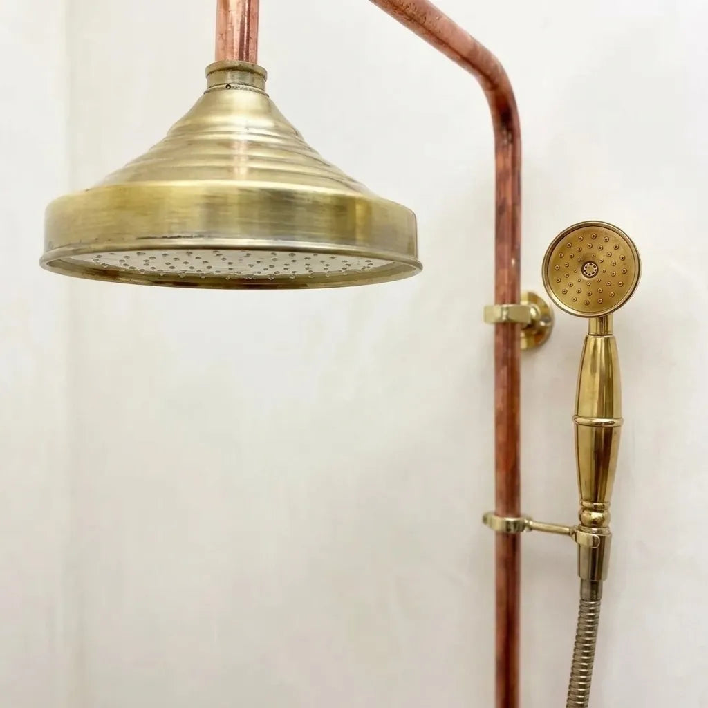 Solid copper exposed shower system with brass rainfall shower head and handheld shower in a minimalist bathroom