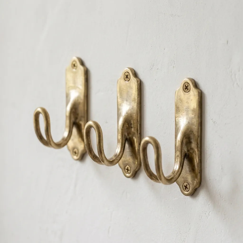 Traditional brass storage hook with graceful curved profile mounted on interior paneling beside a window.