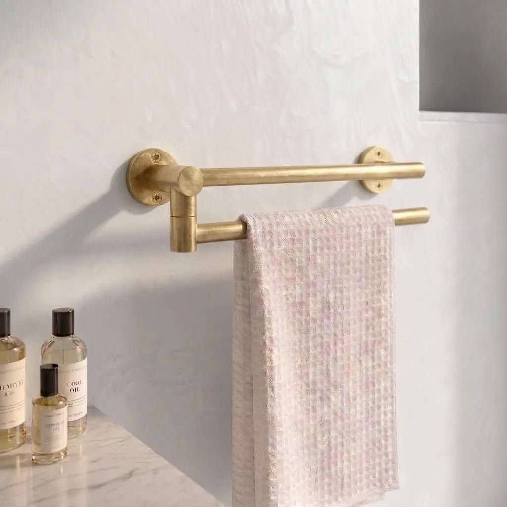 Wall-mounted unlacquered brass double swivel towel bar with independently rotating arms holding a soft waffle bath towel in a modern bathroom.