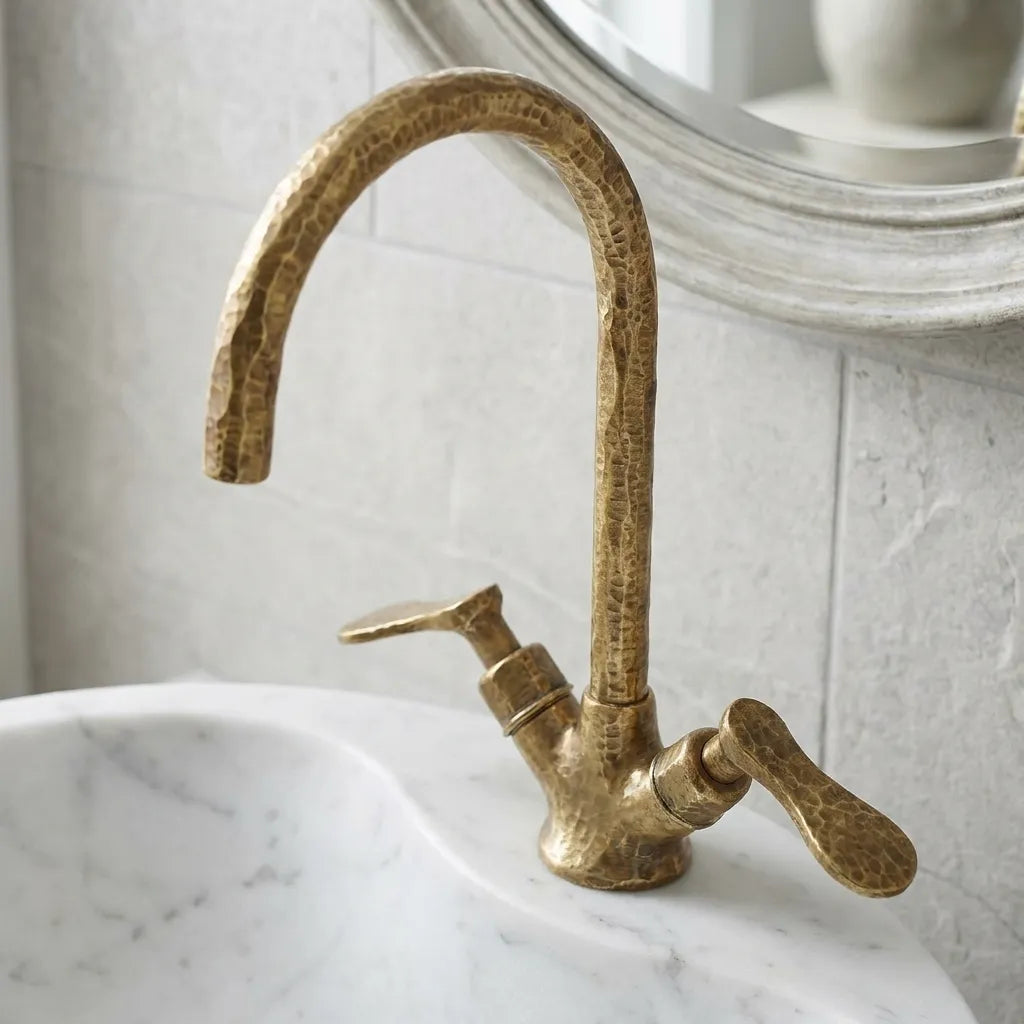 Hammered brass bathroom faucet with high arc spout and sculpted lever handles, mounted on a marble vanity countertop