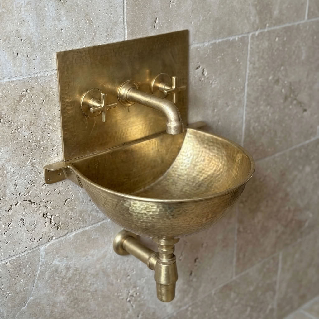 Hammered unlacquered brass wall mounted bathroom sink with brass back plate, cross handle wall faucet and bottle trap