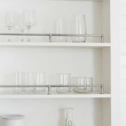 Contemporary chrome shelving rail protecting glass tumblers on open cabinet shelves.