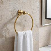 Solid brass wall mounted towel ring holding a white hand towel in a bathroom.