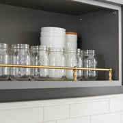 Solid brass gallery shelf rail installed on kitchen cabinet shelf for glass jars and dishes