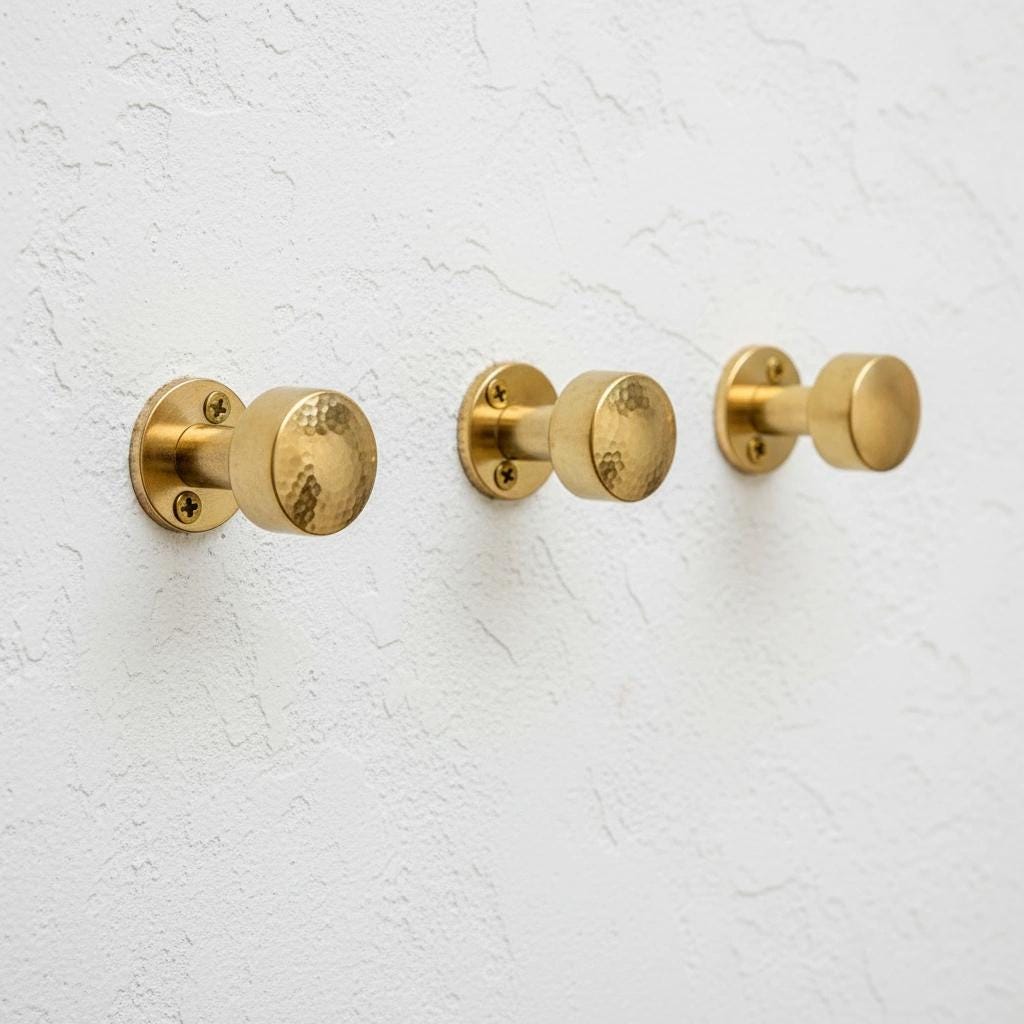 Set of solid brass wall hooks with hammered round knobs for coats, towels, robes, hats, and bags.